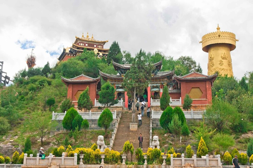 A traditional Chinese temple complex with ornate architecture, a large golden stupa, and a staircase leading up to the temple. 1