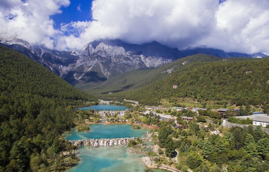 A mountainous landscape with a turquoise lake, a waterfall, and a small settlement. 3