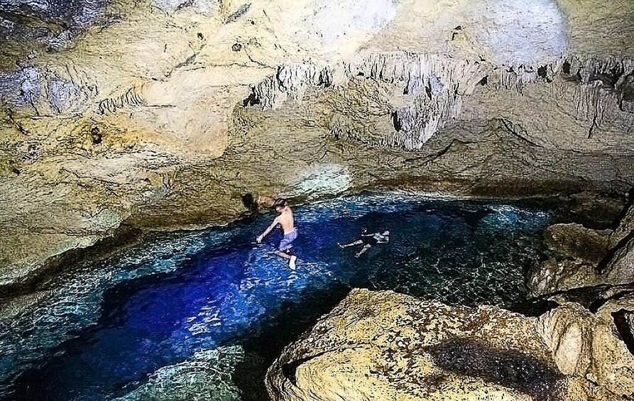 A cave with a pool of water, rocky formations, and a person swimming. 2