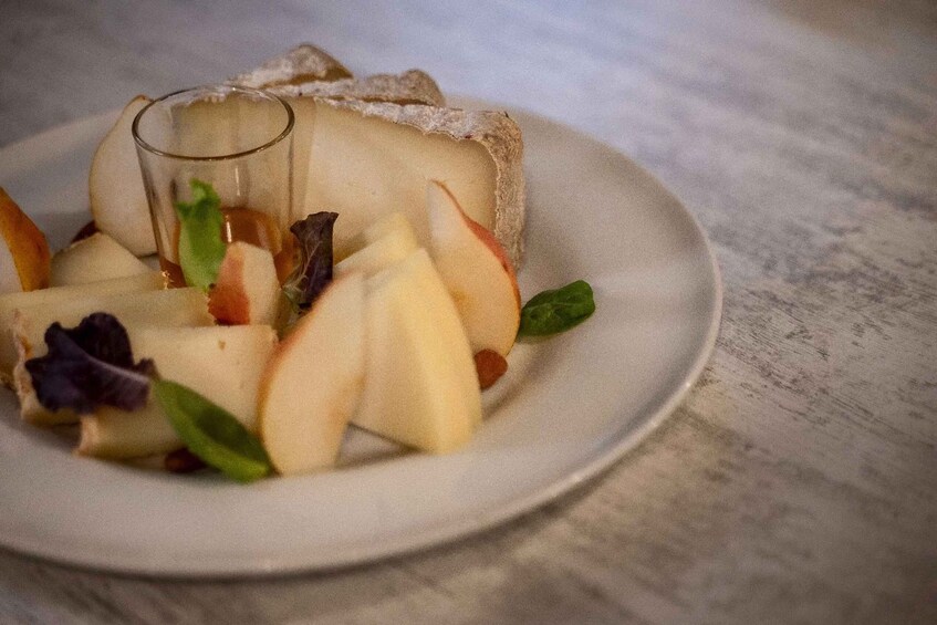 A dessert plate with a slice of cake, apple slices, and a glass of a clear liquid, possibly water or juice, on a textured surface. 1