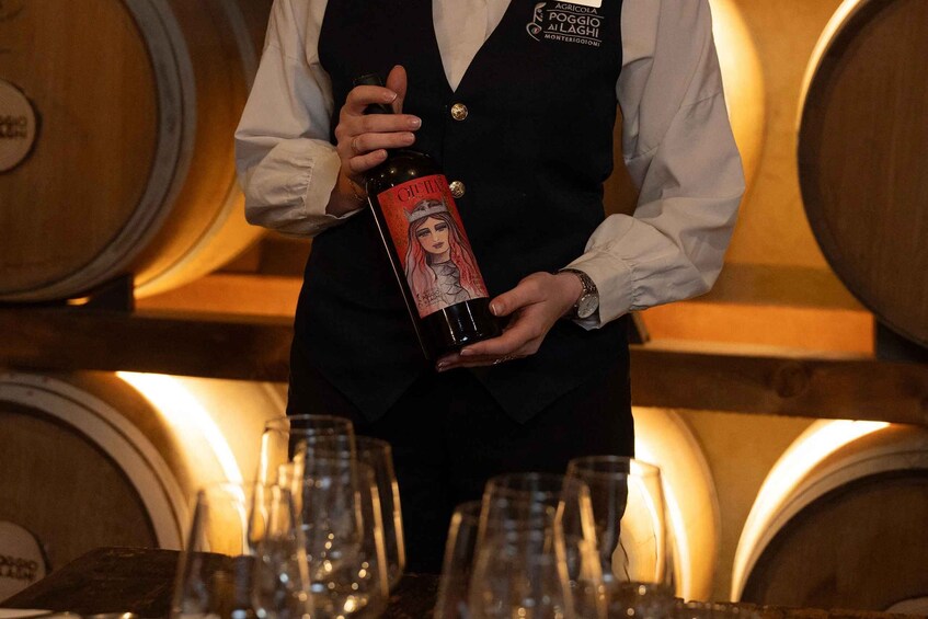 A person holding a bottle with a label, standing in front of wooden barrels. 2