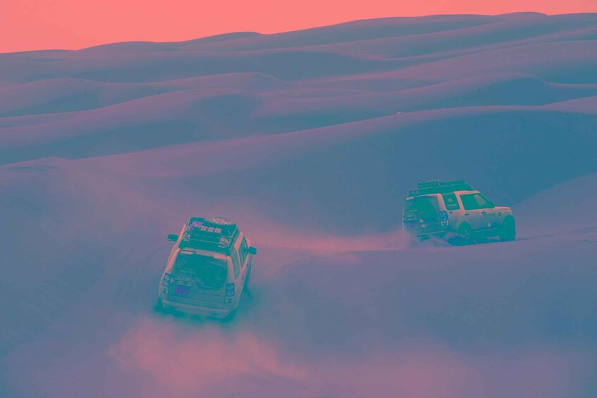 Two off-road vehicles navigating a desert landscape with rolling sand dunes. 2