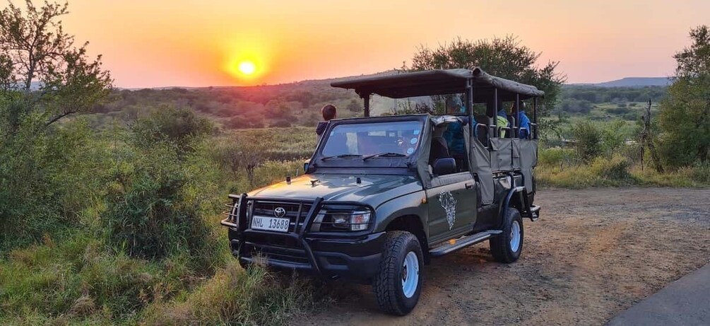 A safari vehicle parked on a dirt road with a sunset in the background. 1