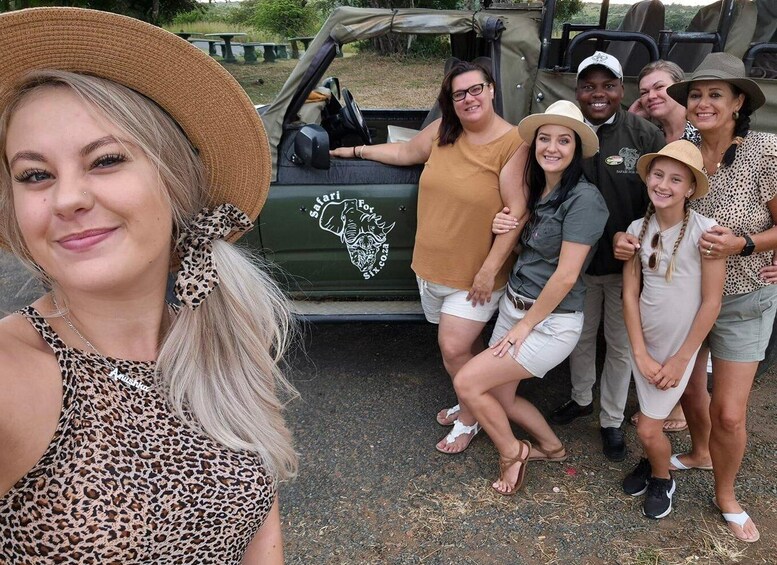 A group of people posing in front of a safari vehicle with a logo of a lion and a giraffe. 3