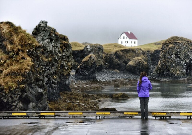 A rocky coastline with a white house on a hill, a person in a purple jacket, and a guardrail. 2