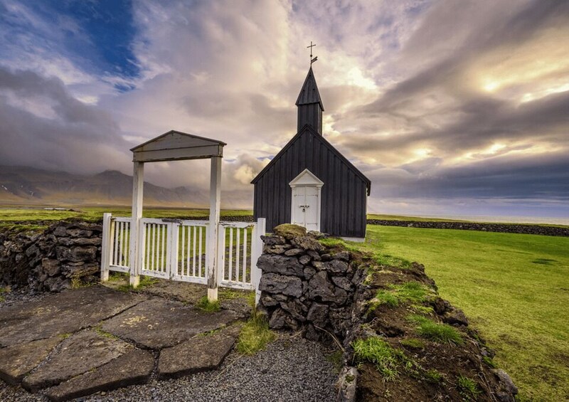 A small church with a white fence and stone walls, set against a cloudy sky. 4