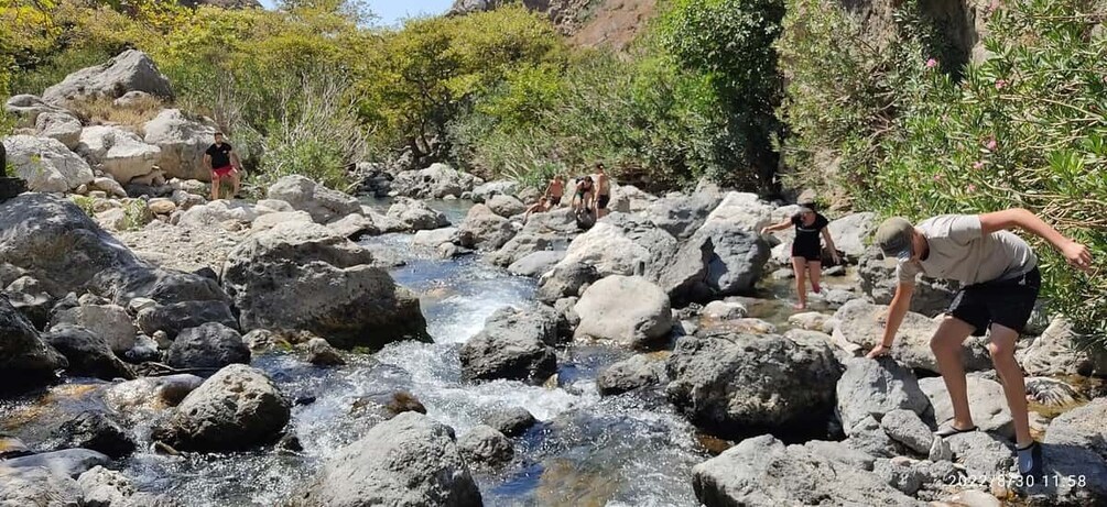 A group of people hiking near a rocky stream in a forested area. 2