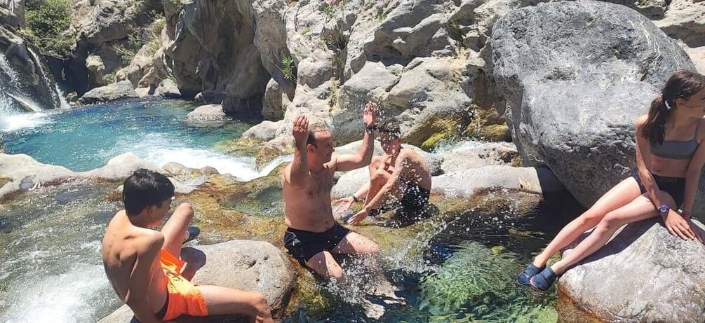 People sitting and standing by a clear water body surrounded by rocks. 5