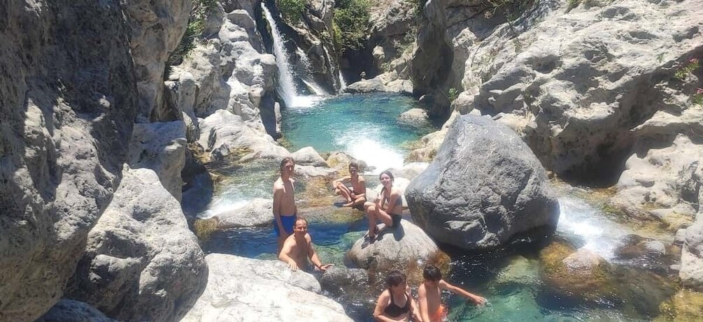 A group of people enjoying a natural hot spring surrounded by rocky terrain and a waterfall. 3