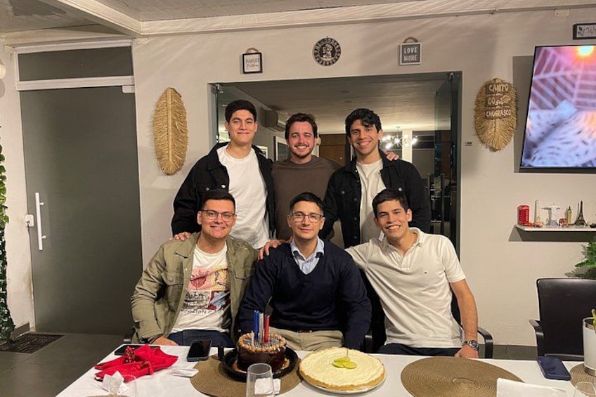 A group of people at a birthday party with a cake on a table. 2