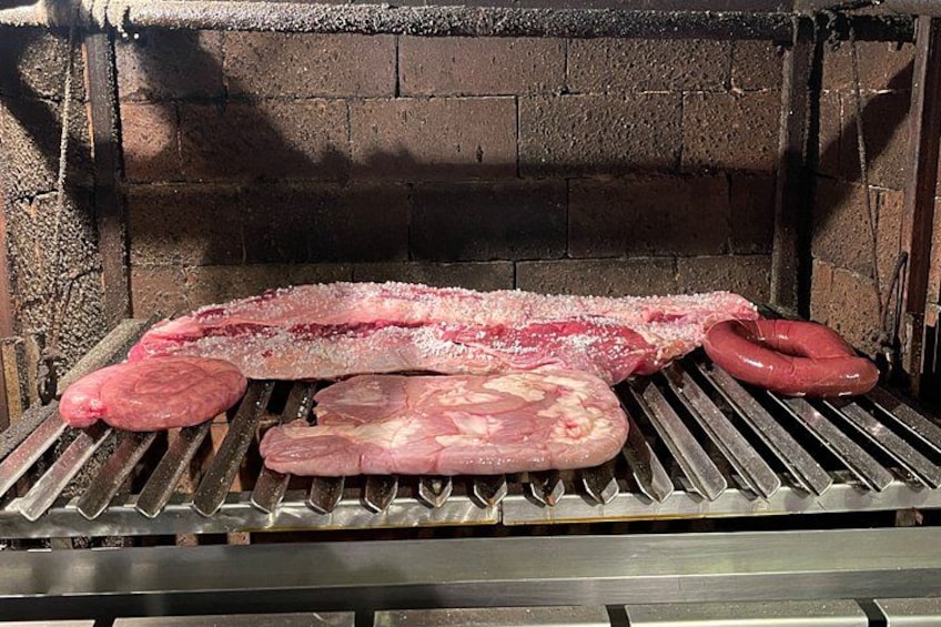 A meat grilling setup with sausages and a large piece of meat on a grill. 5