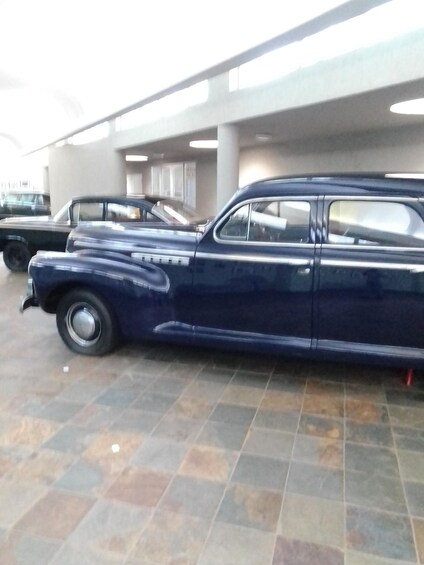 A vintage car parked indoors with a tiled floor and a ceiling with lights. 2