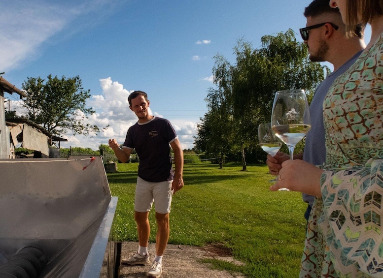 A man standing next to a grill, holding a glass of white wine, with a woman in the foreground. 4