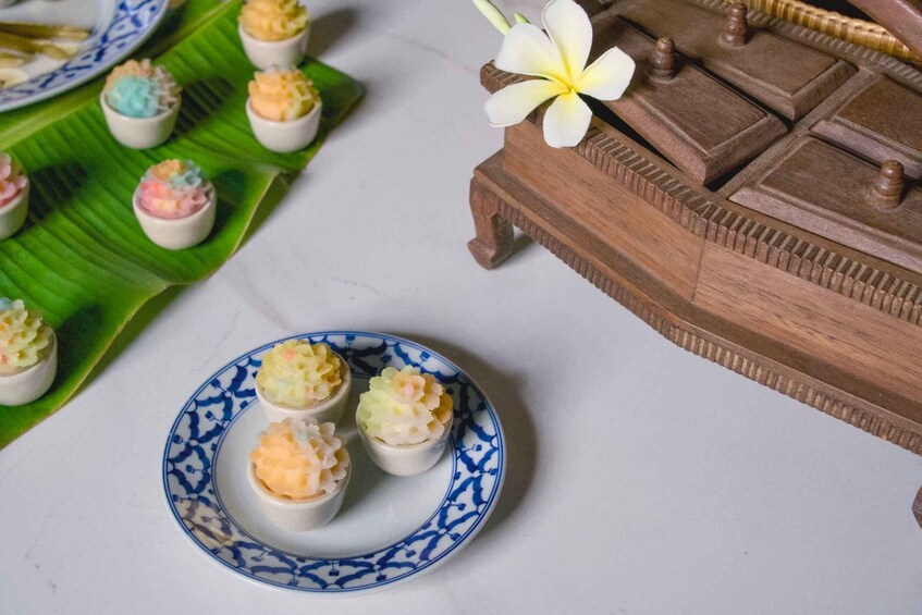 A table with a blue and white patterned plate holding three small cups of food, a banana leaf, and a wooden tray with a flower. 4