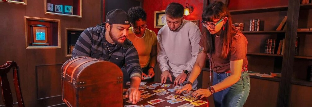 Four people playing a card game at a table with cards and a drum. 1