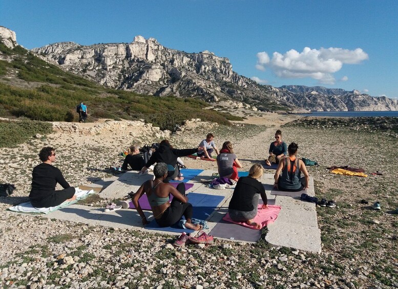 A group of people practicing yoga on mats on a rocky beach with a mountainous backdrop. 4