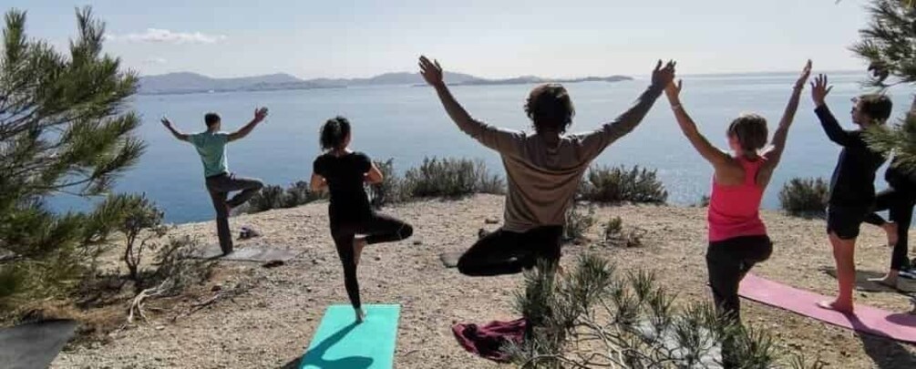 People practicing yoga on mats by a lakeside with trees and mountains in the background. 1