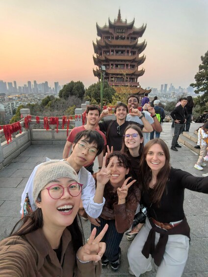 A group of people posing in front of a traditional multi-tiered pagoda with a cityscape in the background. 3