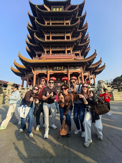A group of people posing in front of a traditional multi-tiered pagoda with Chinese characters. 1