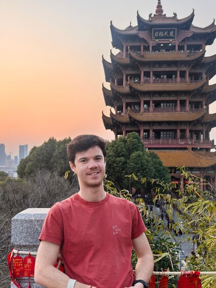 A person standing in front of a traditional multi-tiered pagoda with red decorations and a city skyline in the background. 2