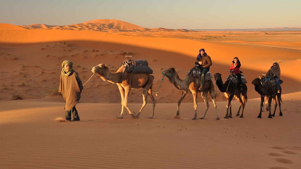 A group of people riding camels across a desert landscape with sand dunes. 3