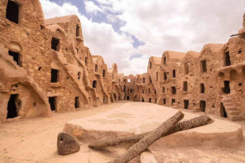 An ancient stone structure with multiple arched doorways and windows, surrounded by a sandy environment. 2