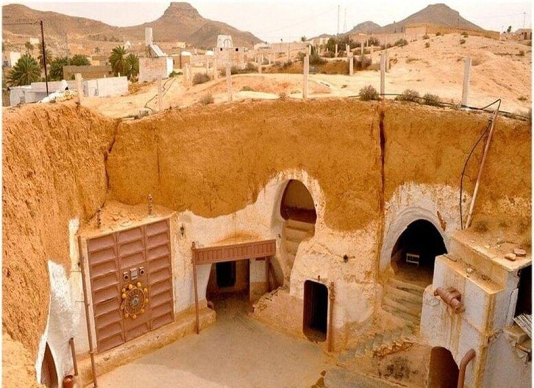 A desert landscape with a large, earthen structure featuring multiple doorways and a central control panel. 1
