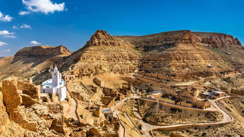A white church amidst ancient ruins, surrounded by terraced structures and a rugged mountainous landscape. 3