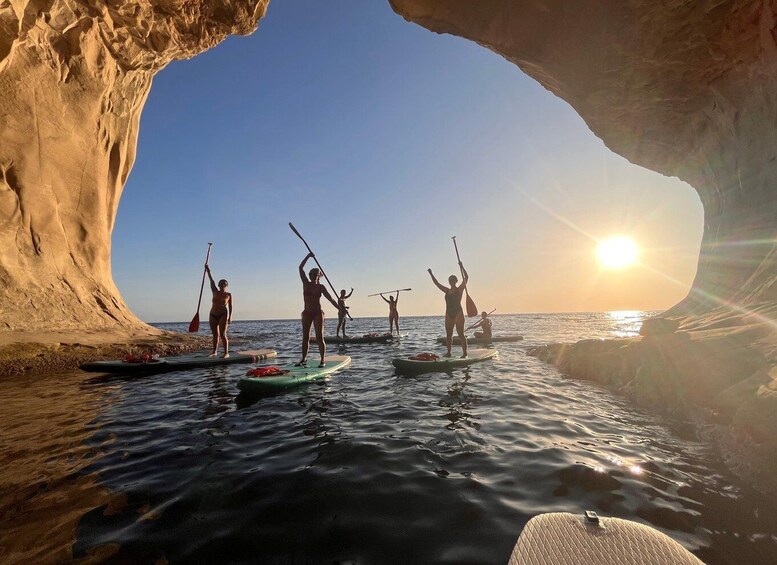 People paddleboarding near a rock formation with the sun setting in the background. 1