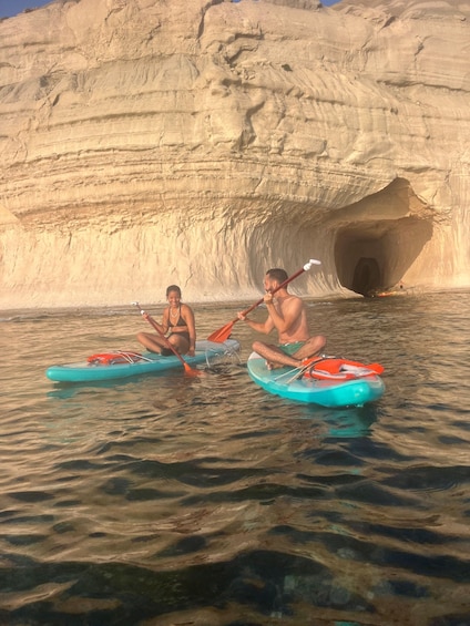 Two people kayaking in a calm body of water with a large rock formation in the background. 2