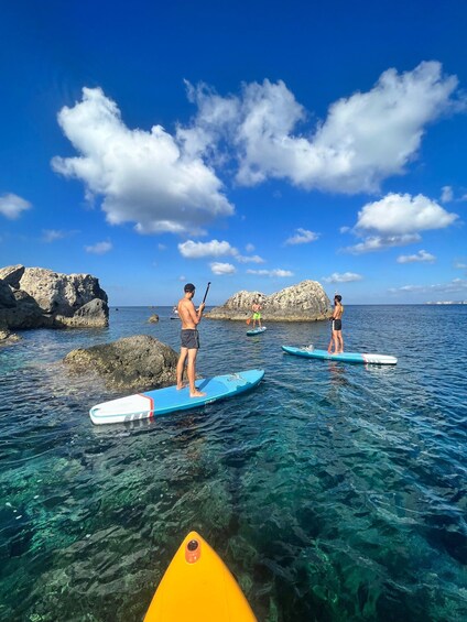 People paddleboarding on clear water with rocky formations in the background. 4