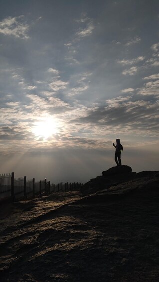 A person standing on a rock with a smartphone, with a fence and a sunset in the background. 4