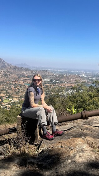 A person sitting on a rock with a scenic view of a city and mountains in the background. 2
