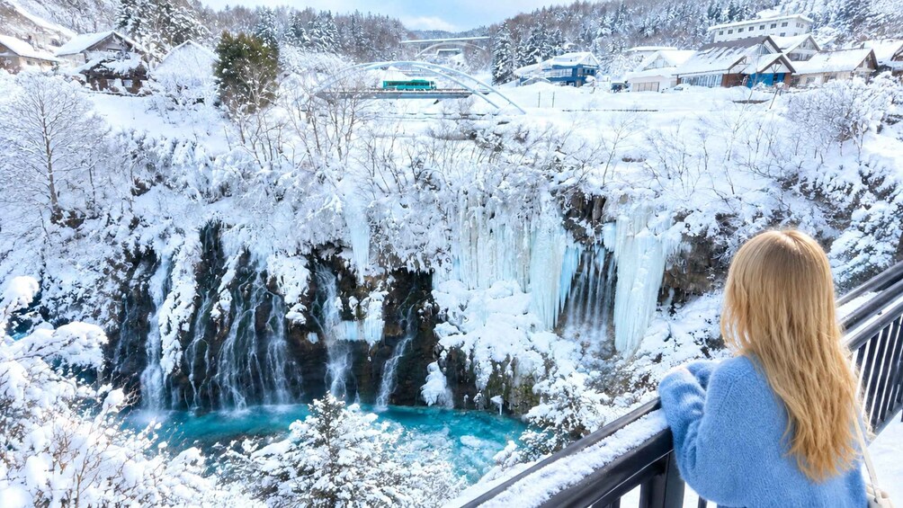 A snowy landscape with a waterfall and a person overlooking it. 2