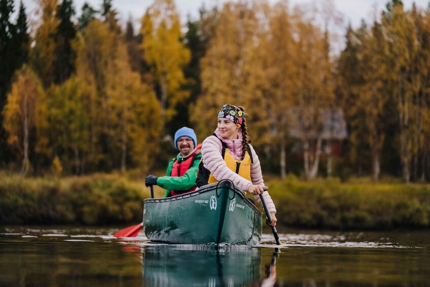 Two people paddling a green canoe on a river surrounded by autumn trees. 1