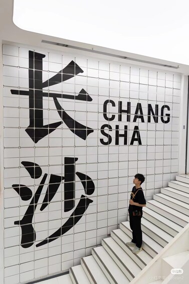 A person standing on a staircase in front of a wall with large Chinese characters and the word 'CHANG SHA' written in English. 3