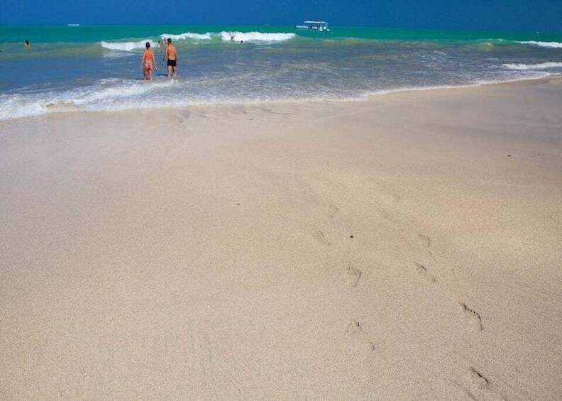 A sandy beach with footprints and two people walking towards the water. 5