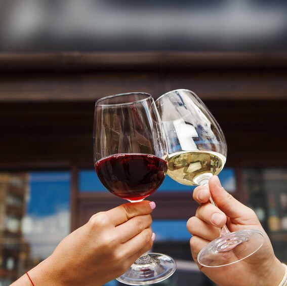 Two hands holding wine glasses, one with red wine and the other with white wine, against a blurred background. 1