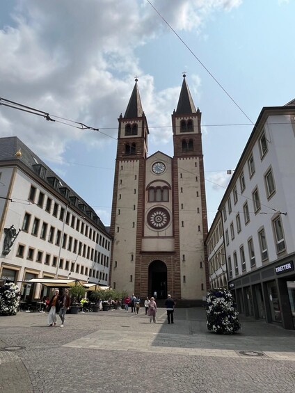 A historic building with a clock tower and two spires, surrounded by cobblestone streets and pedestrians. 3