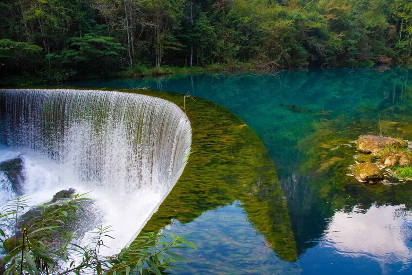 A waterfall cascading into a clear, greenish lake surrounded by dense forest. 5