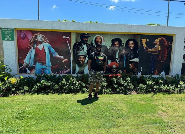 Un murale raffigurante diverse figure, una zona erbosa e un cartello che indica un punto di raccolta di emergenza. 1