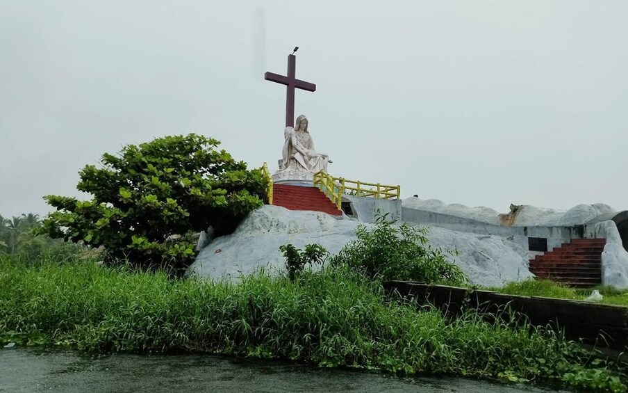 A statue of a figure with a cross, surrounded by greenery and a staircase. 2