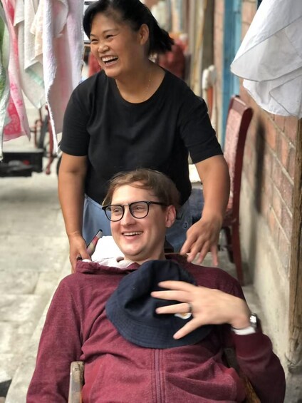 A person seated on a bench, another person standing behind them, and a street with hanging laundry. 5