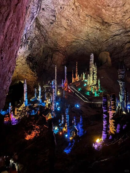 A cave illuminated with colorful lights, featuring rock formations and a central structure. 5