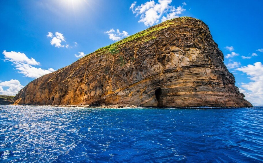 A large rock formation with a cave entrance, surrounded by blue ocean water. 4