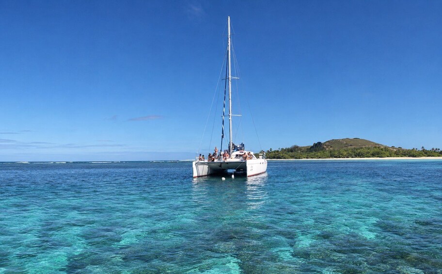 A sailboat on clear turquoise water with a small island in the background. 1