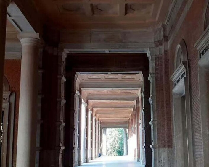 A corridor with columns and arches, leading to a bright area. 1