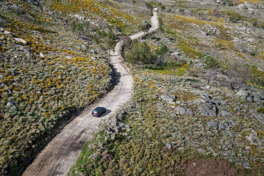 A dirt road winding through a rocky, hilly landscape with sparse vegetation and a vehicle traveling along it. 5