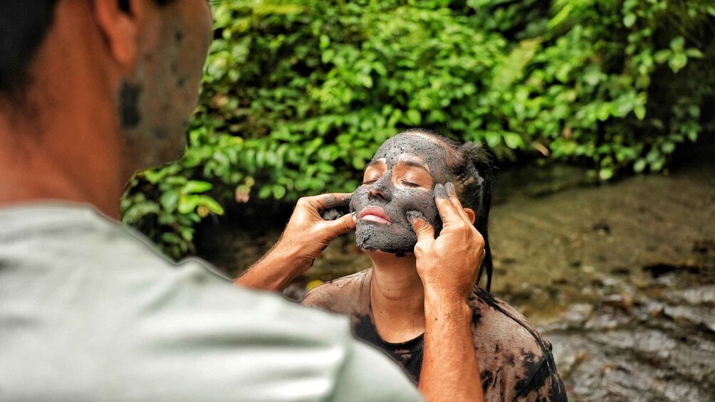 A person applying mud to their face outdoors. 4