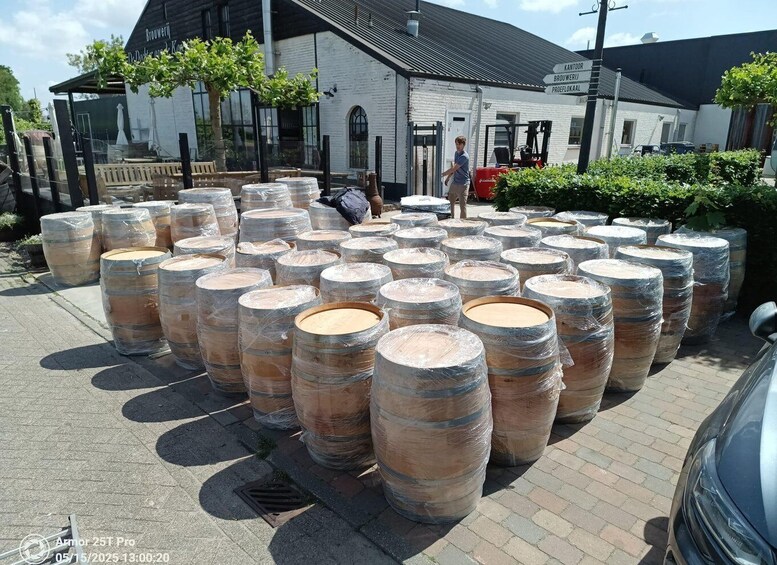 Large wooden barrels wrapped in plastic, stacked in rows, outside a building with a sign that reads 'Brouwerij De Dokkstraat'. 3